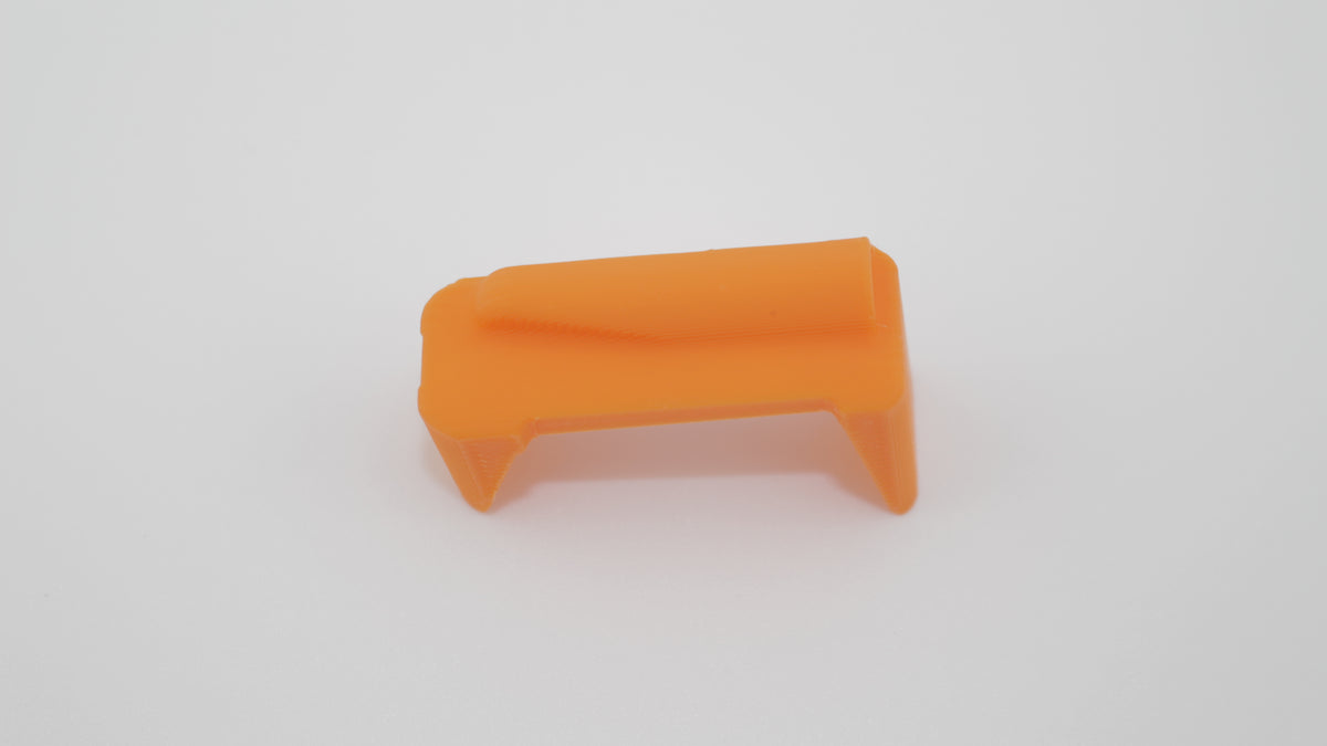 Top view of orange anti‑tilt magazine follower for M1 Carbine, featuring angled top ramp and rectangular body on light gray background